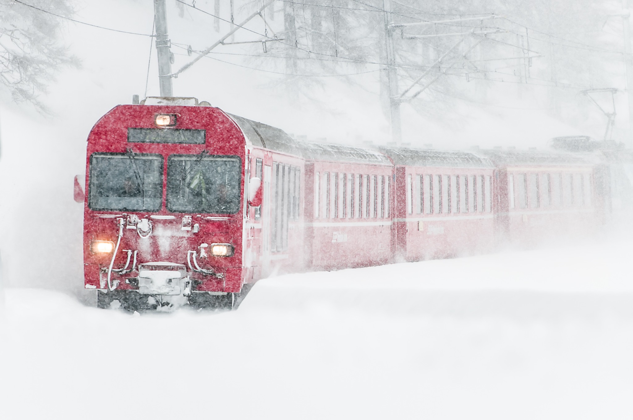 Red train travelling through a winter snowstorm